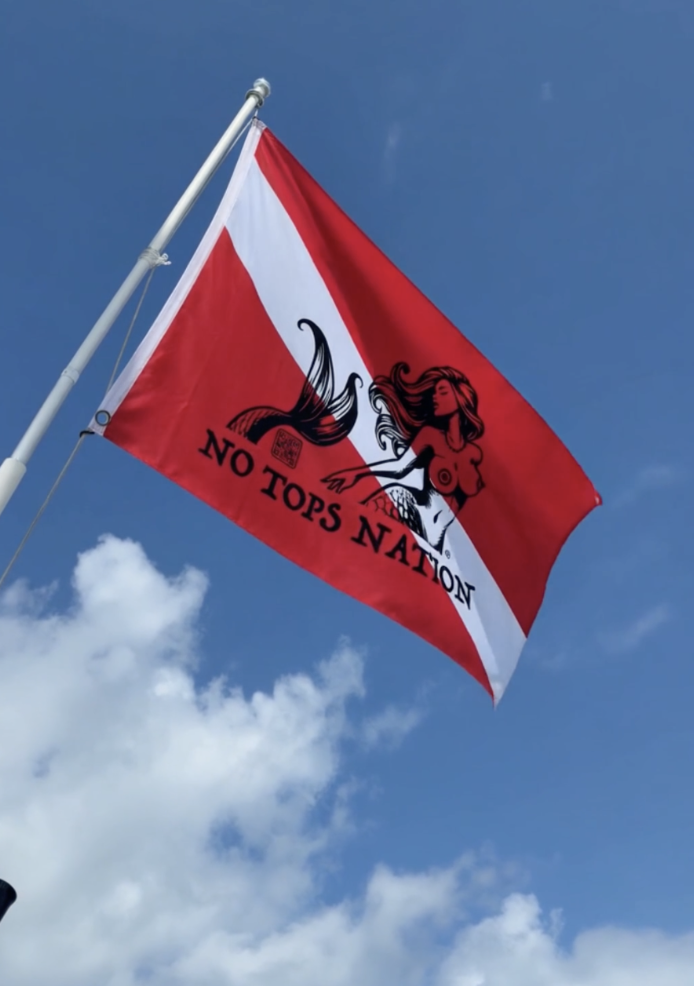 Close-up of the No Tops Nation double-sided dive boat flag flying against a bright blue sky.