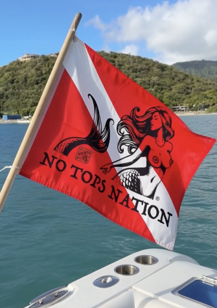 No Tops Nation double-sided marine dive boat flag flying from the stern of a boat on clear blue tropical water.